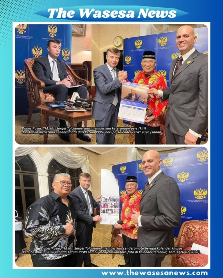 Tolchenov menerima cenderamata kalender PPWI 2026 dari Wilson Lalengke (Ketum PPWI), sekaligus memberikan kalender khusus Kedubes Rusia 2026 sambil menjelaskan foto-fotonya, dengan beberapa tamu undangan yang hadir.