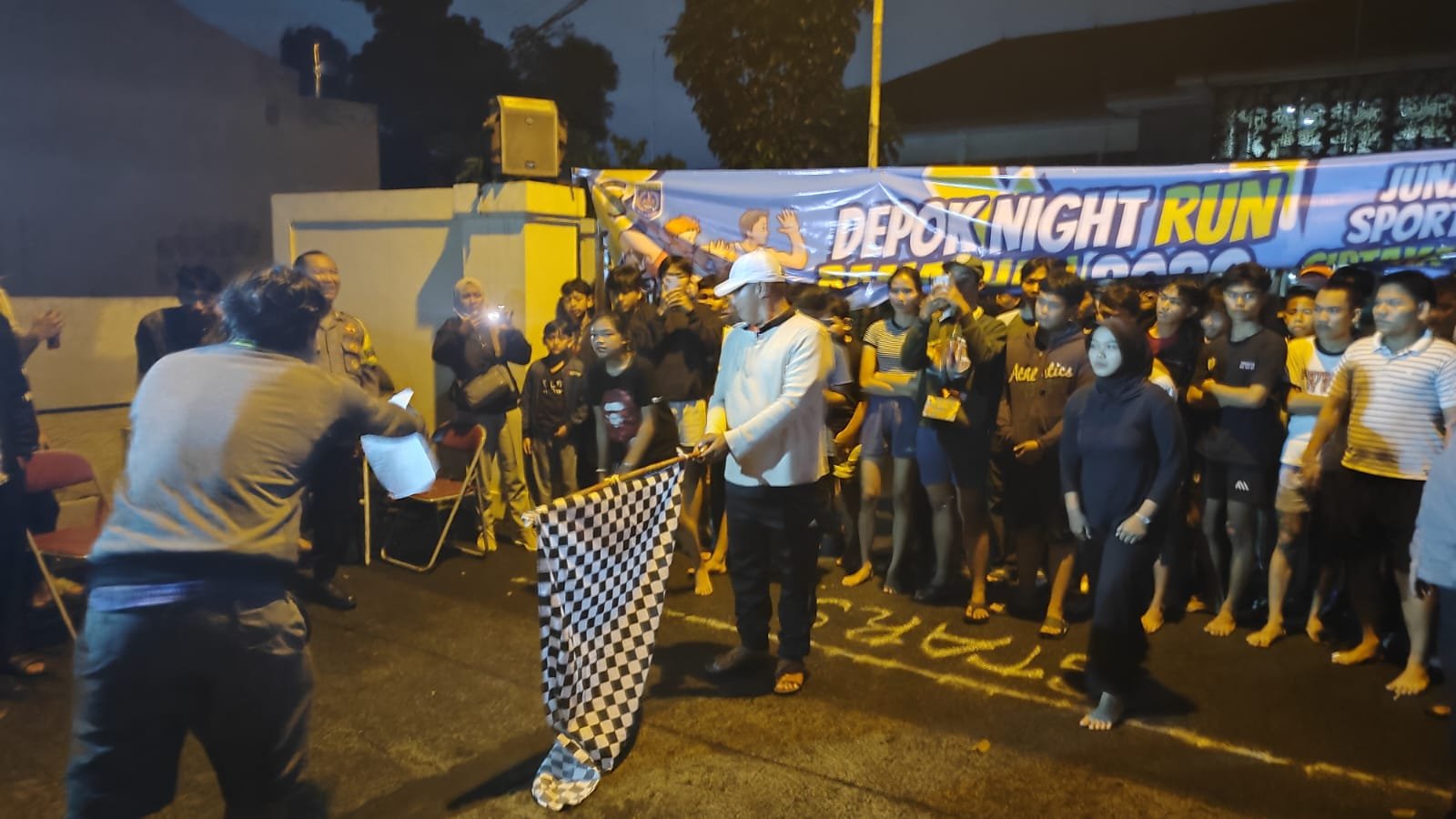 Para peserta Depok Night Run Ramadhan 2026 bersiap memulai perlombaan di depan titik start Jalan Kantor Kecamatan Limo, didampingi oleh personel Polsek Cinere dan petugas acara.