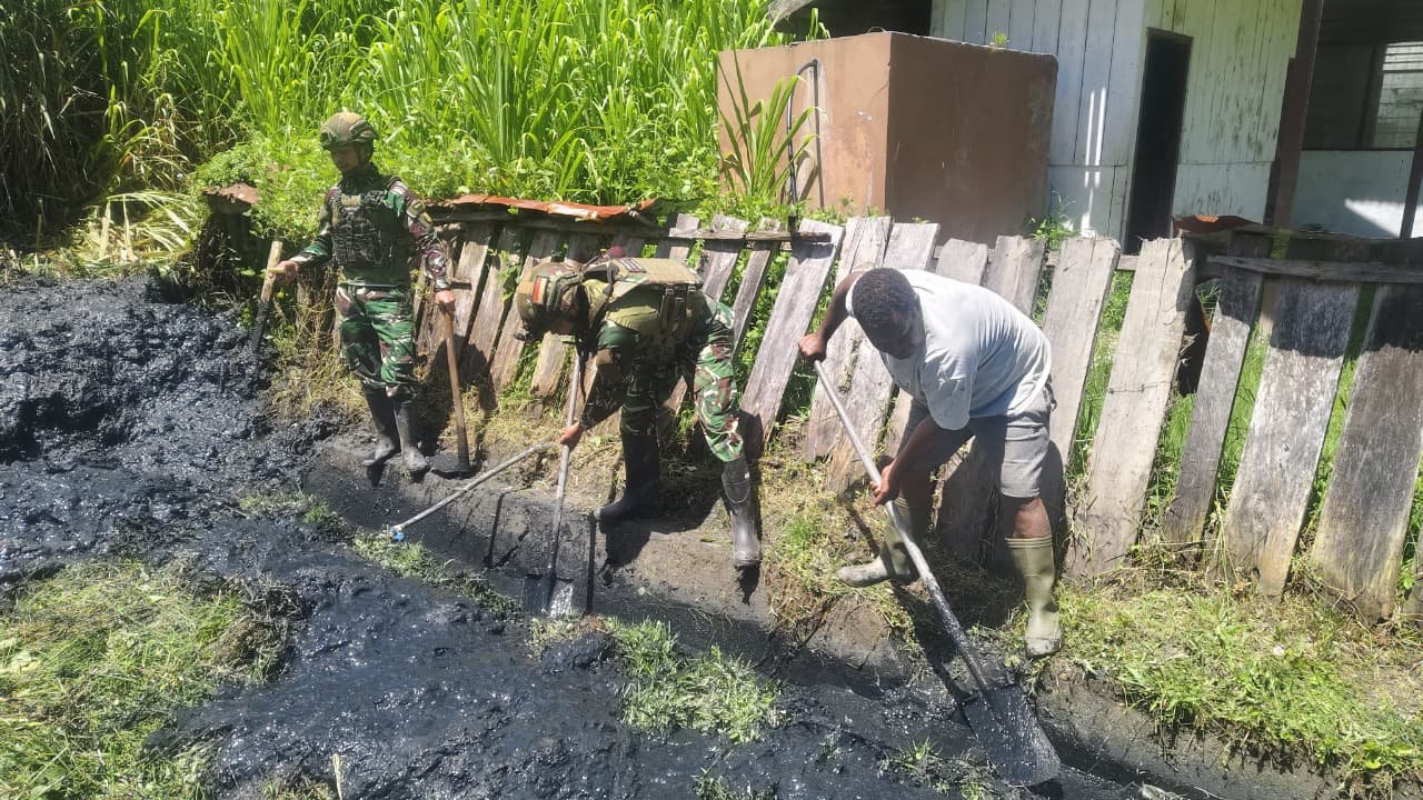 Personel Satgas Yonif 521/DY bersama warga Distrik Kurima Yahukimo saat melakukan aksi gotong royong membersihkan jalan dan selokan kampung. - thewasesanews.com
