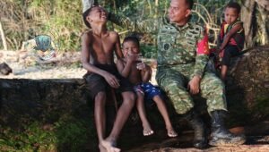 Dandim 1801/Manokwari Letkol Inf Davit Sutrisno Sirait saat duduk bersama anak-anak Kampung Tanah Rubuh di tepi pantai dalam pelaksanaan TMMD Ke-128. - thewasesanews.com